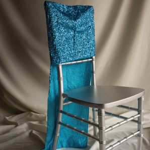 Blue sequined chair cover on a silver colored Chiavari chair in front of a white back drop.