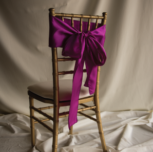 Back of a magenta colored chair sash tied into a bow on a silver chair.
