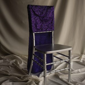 Purple sequined chair cover on a silver colored Chiavari chair in front of a white back drop.