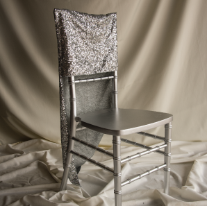 Silver sequined chair cover on a silver colored Chiavari chair in front of a white back drop.