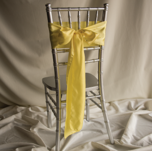 Back of a yellow chair sash tied into a bow on a silver chair.